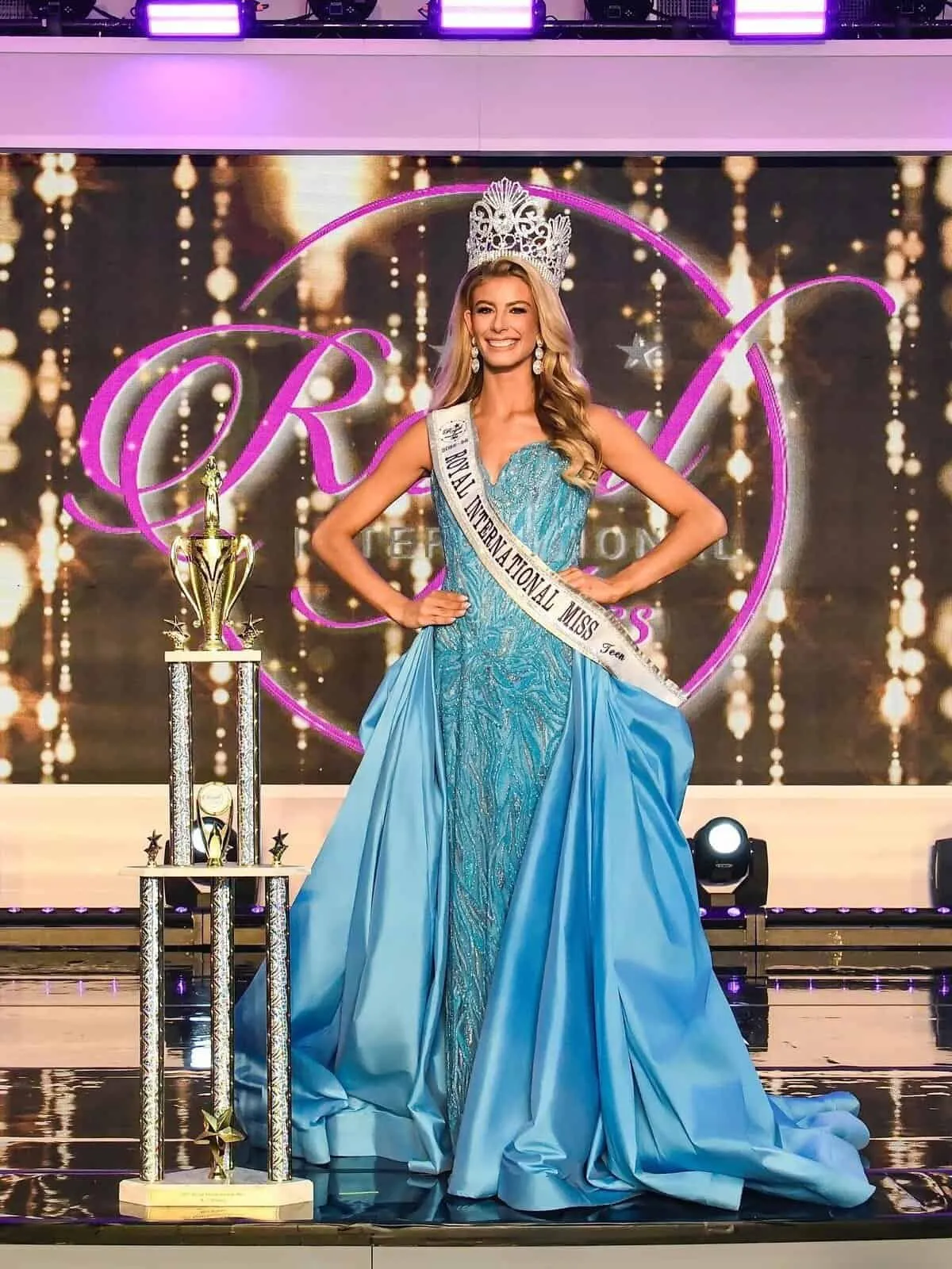 Ilané Liebenberg crowned on the Royal International Miss stage, in a sky-blue gown beside her trophy