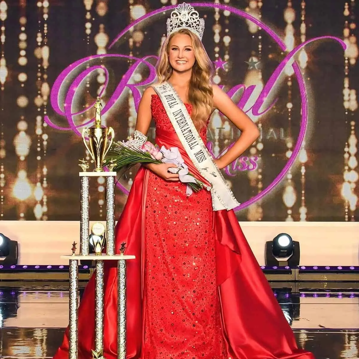 Juané van Rooyen crowned on the Royal International Miss stage, in a red gown beside her trophy