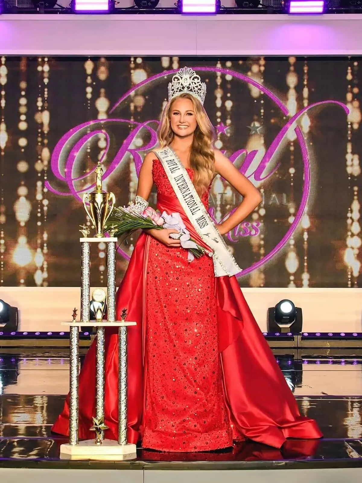 Juané van Rooyen crowned on the Royal International Miss stage, in a red gown beside her trophy