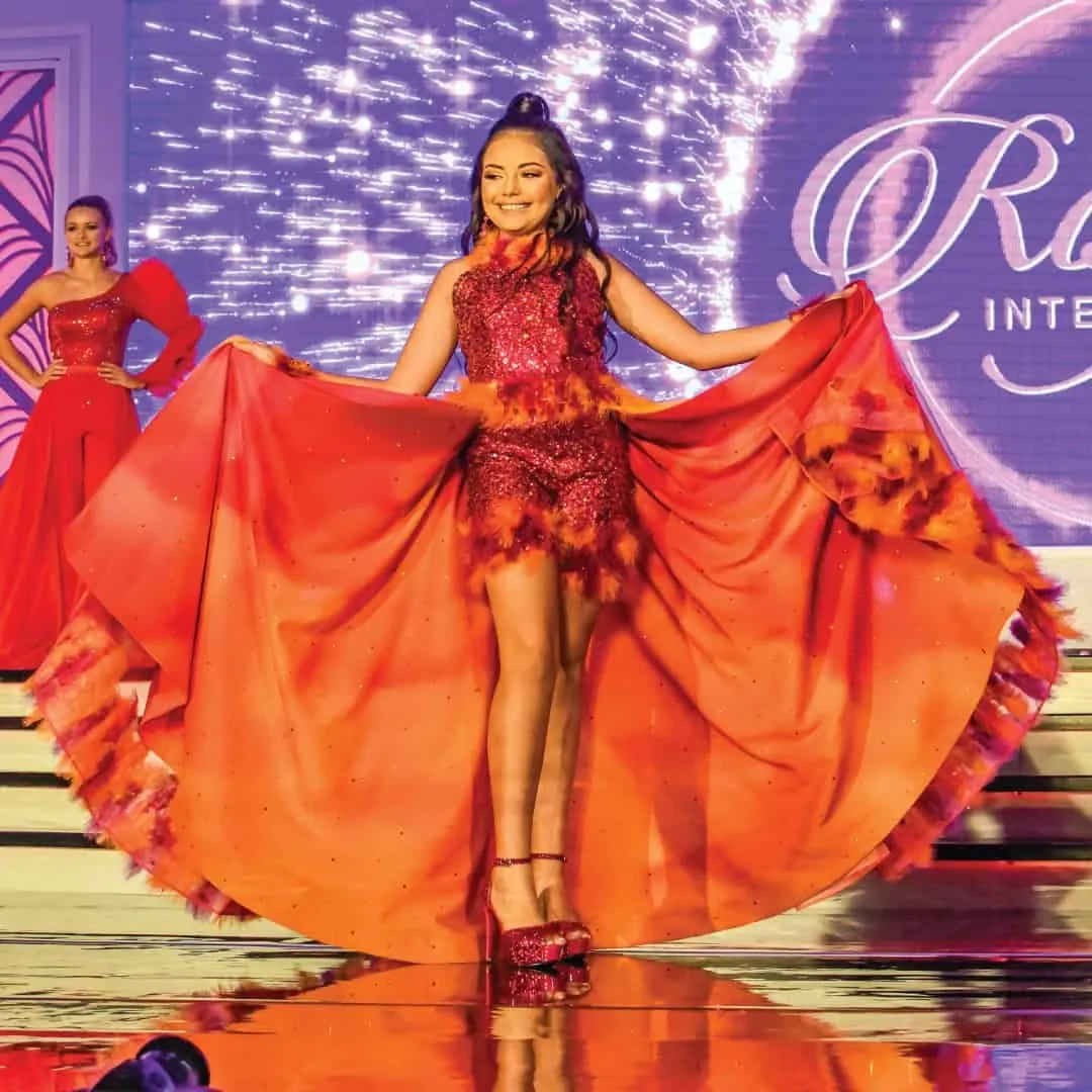 A delegate in a flowing red gown spreading her skirt on stage