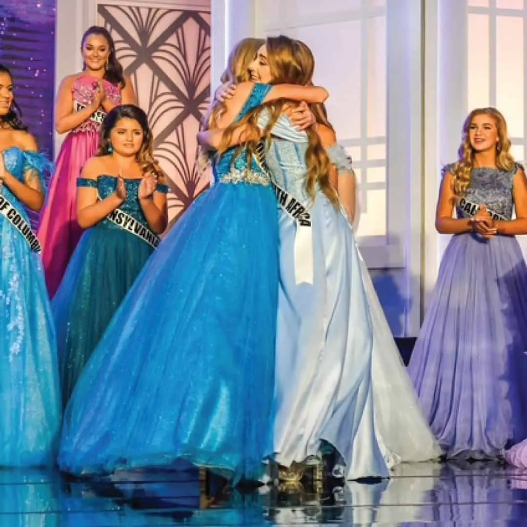 Delegates in blue gowns hugging on stage after the crowning