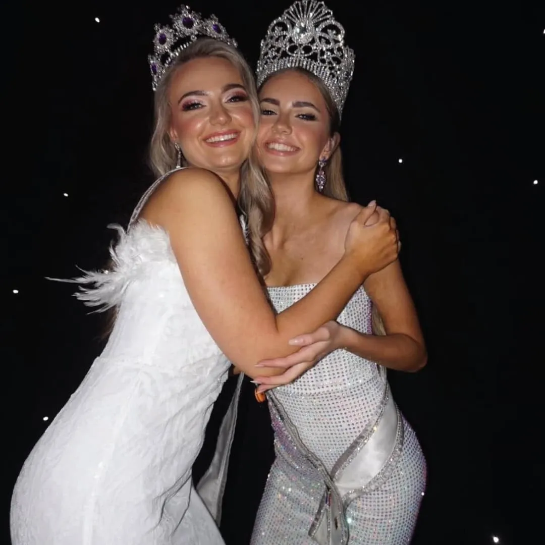 Two crowned delegates in white embracing at the international pageant
