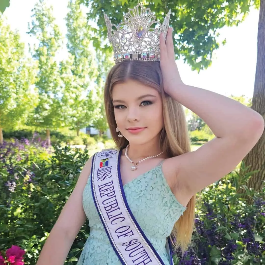 A young South African delegate wearing her crown and sash in a garden